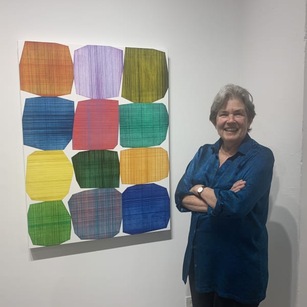 Woman standing next to a colorful, geometric, abstract painting hanging on a gallery wall.