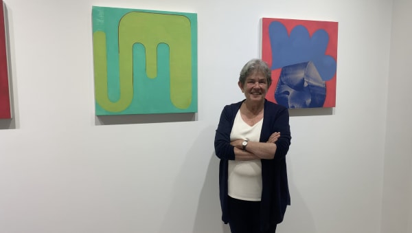 Woman standing in front of two colorful, bold abstract paintings on gallery wall.