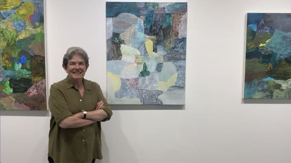 Woman standing in front of three abstract art paintings.