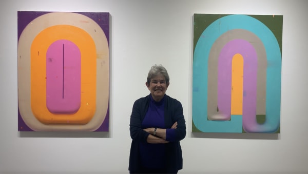 Woman standing between two colorful, geometric paintings on wall.