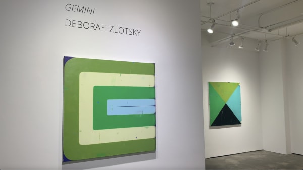 Two green, blue, yellow, and black abstract paintings on gallery walls