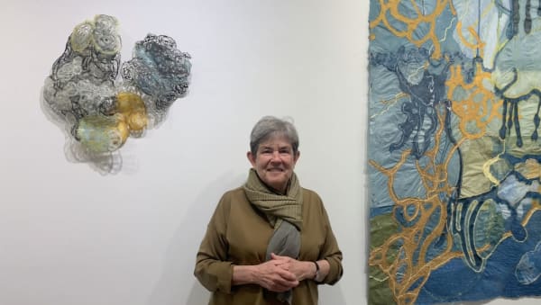 Woman standing in front of a glass wall sculpture and work on paper.