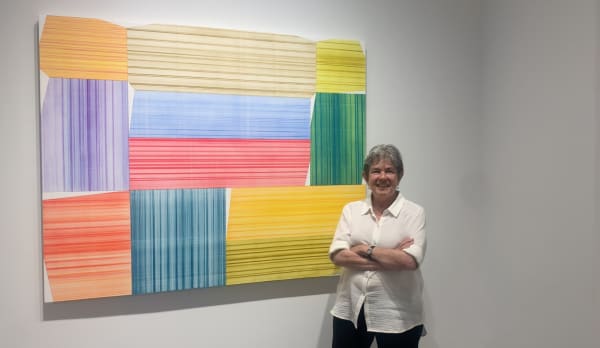 Woman standing in front of large abstract painting with colorful polygons.