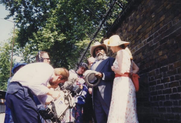 Rebecca Hossack and Clifford Possum Tjapaltjarri being filmed by a camera crew outside Buckhingham Palace.