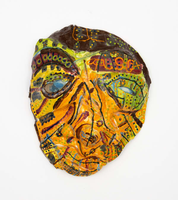 A highly decorated abstract ceramic mask with a bright yellow background blending into green at the eyes and strip of black with decorative dot patterns at the top. The eyebrows and eyes are bold. Dark lines and gestural marks with lines of dots to the ou