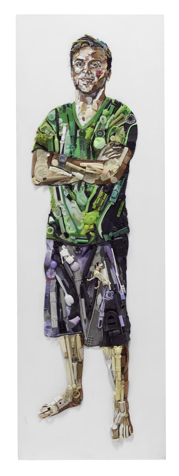 A portrait of a twenty two year old white man standing. He is wearing a green t-shirt and grey-purple shorts and is barefoot. His arms are crossed in front of him in a confident stance. He is smiling a friendly smile. The materials used for the color pallet are strictly ocean plastic pollution collected from beaches, mostly Marin County beaches. The background is painted white with acrylic paint. The ocean plastic has been cut to fit in some areas but there is no paint on the plastic.