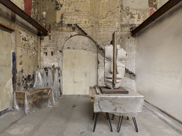 image of Mark Manders installation with split clay head on table and large dry clay head with plastic