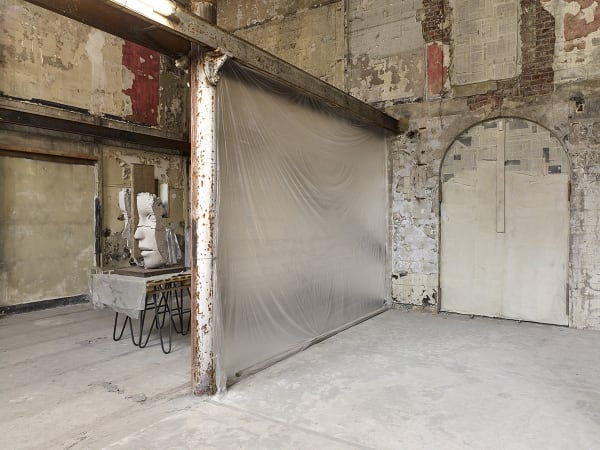image of Mark Manders installation with split clay head on table and large dry clay head with plastic