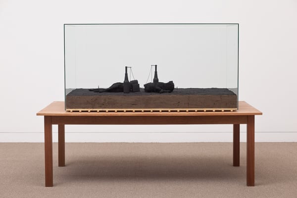 Image of Mark Manders sculpture with dark table and glass case