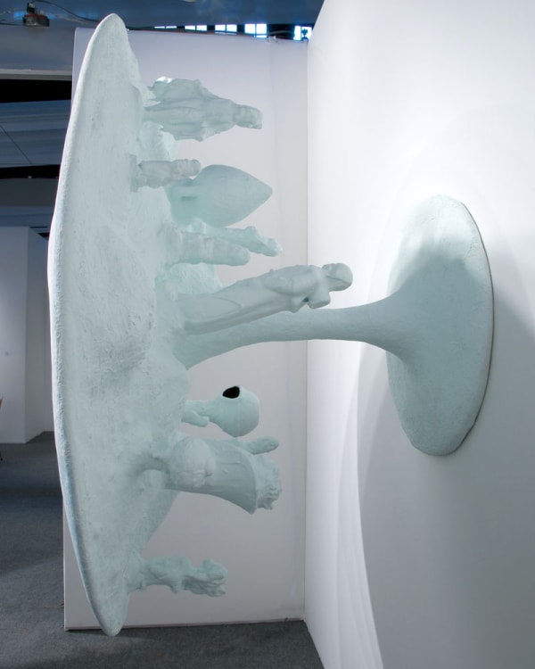 image of table-like sculpture mounted on wall with abstracted forms coming out from underneath the table