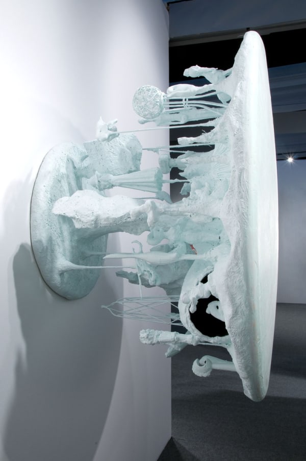 image of table-like sculpture mounted on wall with abstracted forms coming out from underneath the table