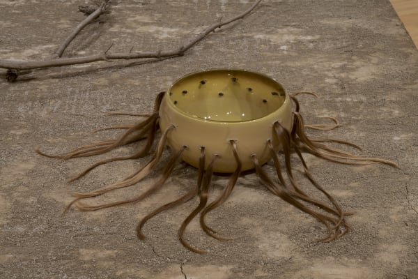 a ceramic sculpture with hair bundles extruding, on an earthen platform
