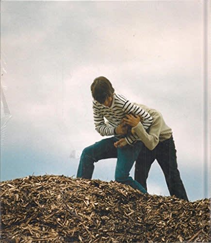 Exhibition catalogue cover for Phill Collins exhibition "Yeah, you, baby you". Two boys tussle on top of a pile of woodchips. Boy wearing a striped sweater has the other in a headlock.