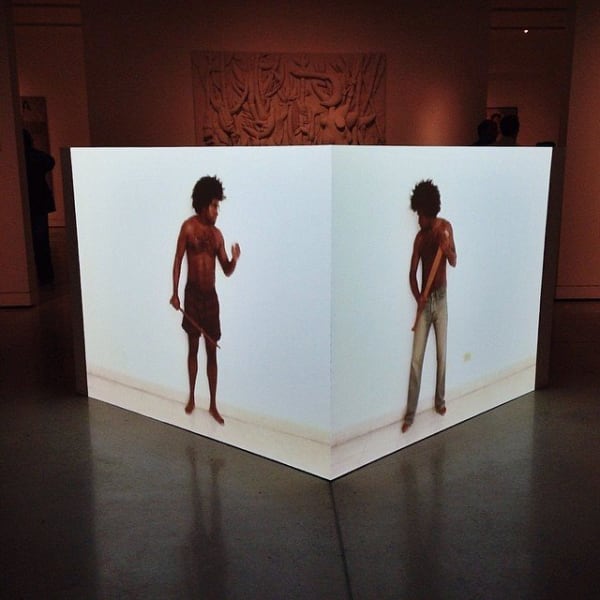 A white cube sits in the centre of the room. Two figures are projected onto different walls of the cube, facing each other.