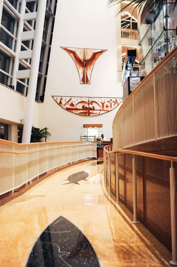 Photograph of a corridor with wooden floors and walls. A bowl-shaped painting and a painting of a bird hang at the end of the corridor. 