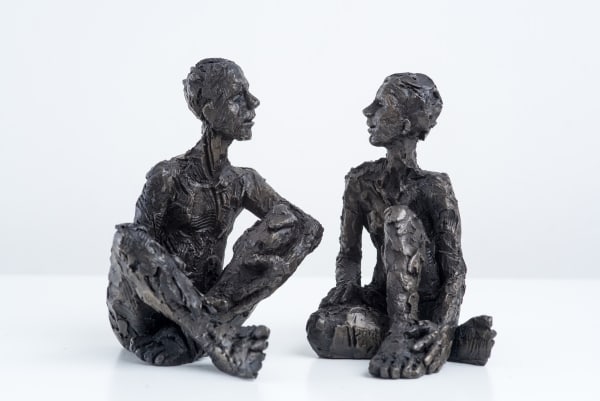 Carol Peace sculptures, a man and a woman, seated with their legs crossed, displayed looking at each other, as if in conversation. Highly textured and the iron resin is almost black.