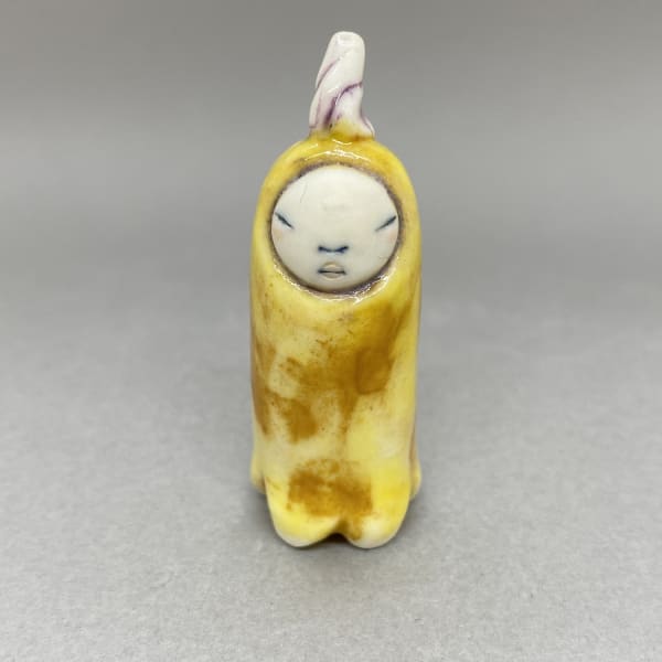 A tiny sculpture of a plant spirit in bright yellow and a purple seedling on its head.