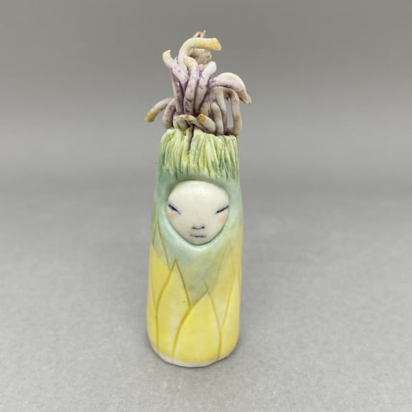 Marina Bauguil tiny figurative sculpture of a plant spirit in yellow and green with a purple seedlings hat.