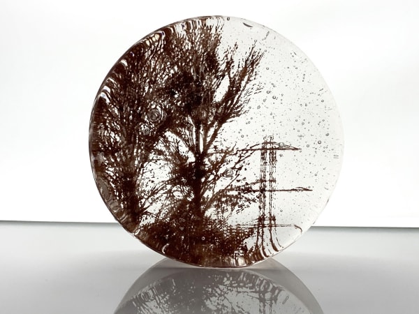 Helen Slater round glass art piece with the image of trees and pylon in sepia against a transparent background.