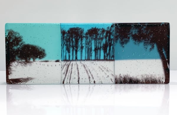Helen Slater rectangular glass art piece with a silhouette of a filed and trees against a blue background.