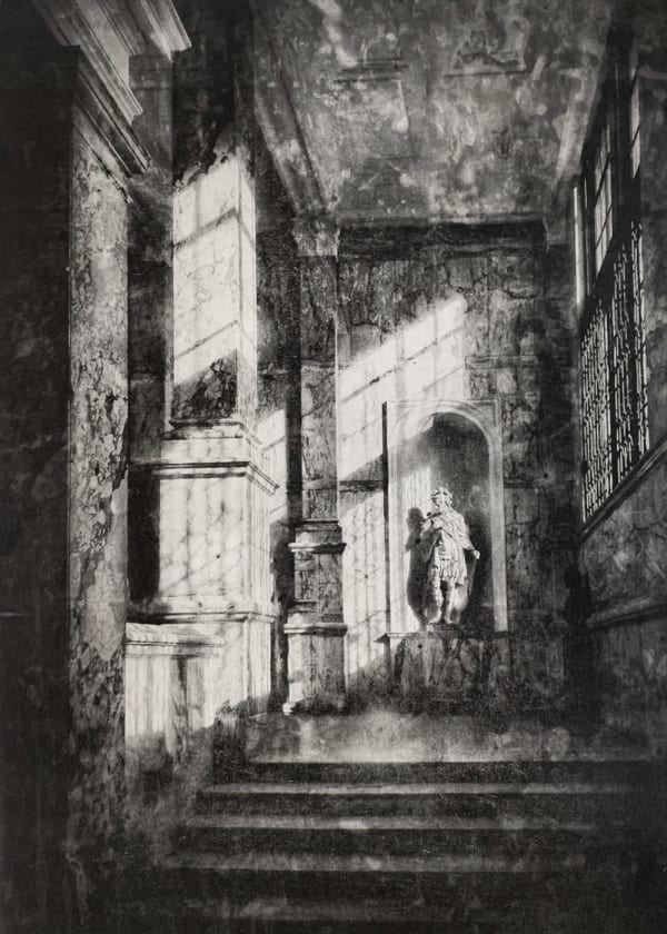 Lindsey Moran tonal print of a view in black and white of a stairwell in a grand Victorian building, a sculpture of a male figure stands on the landing. Light falls from a large window on the right.
