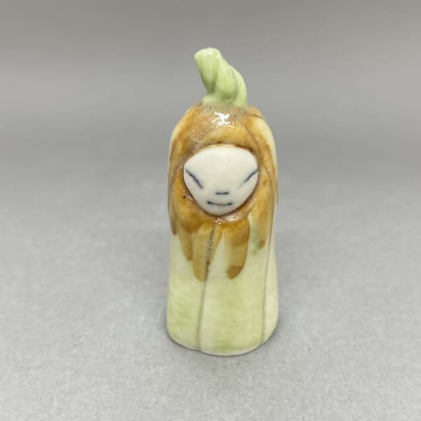 A tiny sculpture of a plant spirit in pale green and an orange hood, a green seedling on its head.