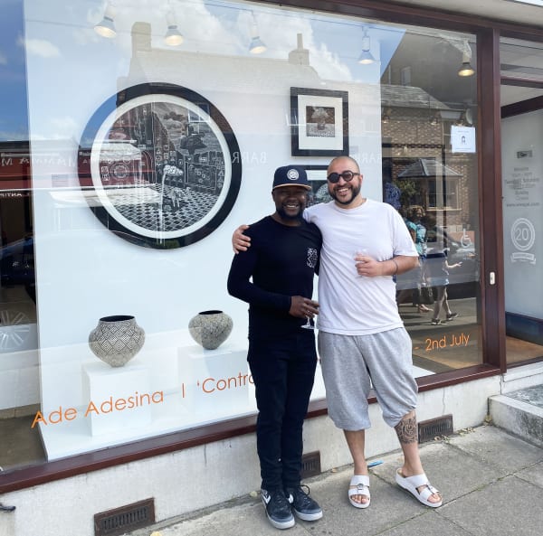 Ade Adesina is standing with the artist Ahmad Ahmad, with their collaborative work 'Twenty Twenty' on show in the window of Sarah Wiseman Gallery