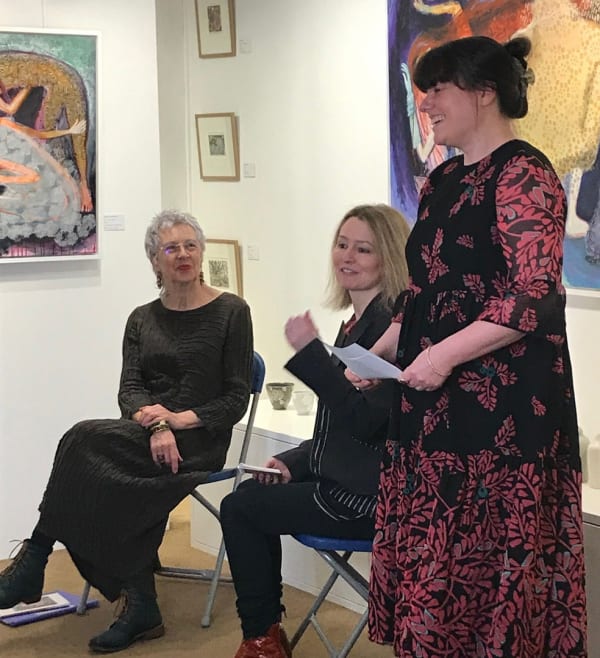 Lesley Saunders sitting with Rebecca Swainston, Sarah Wiseman stands with paper in her hand talking to an audience.