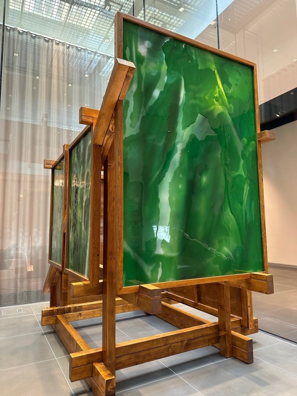 Large mixed-media installation made up of a wooden structure holding five green resin paintings.