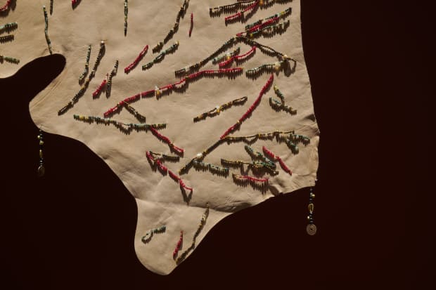 Prologue, 2024, Beaded cow hides hung on antique wooden pillars with aluminium saddles, Dimensions variable.