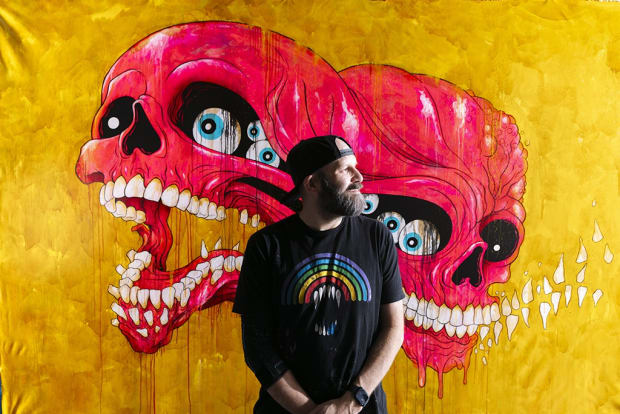 Photo of artist Alex Pardee in front of one of his paintings in his studio