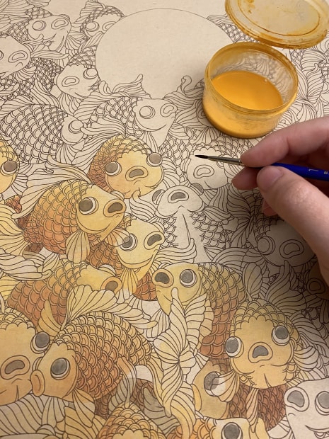 close up photograph of Felicia Chiao painting a group of yellow fish 