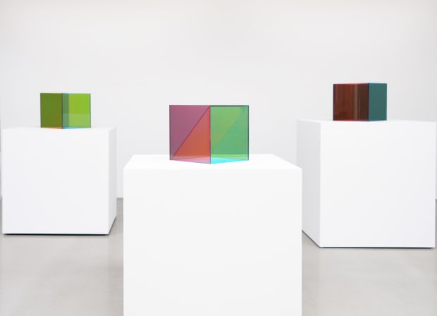 Three cubes made of tinted hues of glass invite viewers to perceive a multitude of color overlaps and mixes and...
