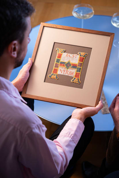 A person holding an illuminated miniature from the Middle Age, sitting on a chair inside of a cozy art gallery.