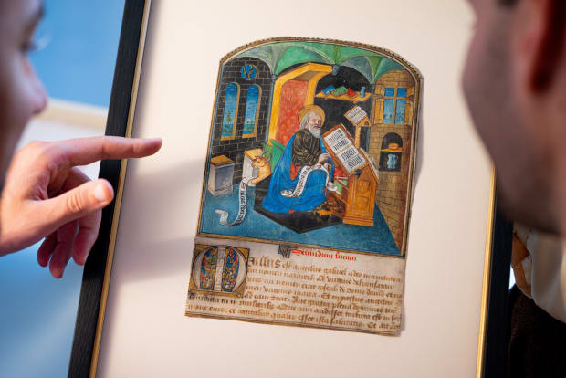 Medieval illuminated manuscript showing Saint Luke in blue robes writing at his desk, with his lion symbol below. Gothic architectural setting with Latin text 'Secundum lucam' underneath.