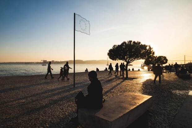 《欧盟旗》,里斯本(葡萄牙),2020 《欧盟旗》是一件位于葡萄牙里斯本的一件 永久公共艺术作品 这个作品展示了一面由铁栅栏和铁丝网制成的欧洲旗帜,这些材料让人联想到移民在试图进入欧洲时面临的物理障碍,以及他们在非人道的难民营中满怀希望地等待的情景。 尽管它探讨的是残酷的现实,但作品也试图传达希望--寻求庇护者的希望。线条创造了一个剪影,让背景中的天空透出来,旨给人以希望的感觉。它位于流入大海的河流前,暗示了他们中的许多人在寻找更好的生活的过程中所经历的和仍在进行的海上航行。 作品在里斯本的Praça Europa(位于Catis do Sodre和Ribeira das Naus之间)展出。里斯本