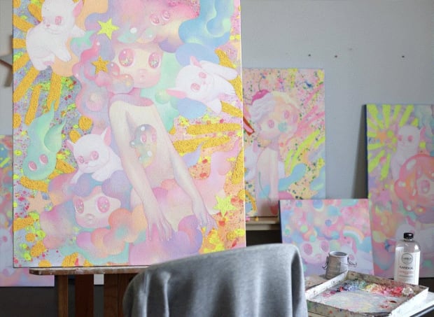 shot of So Youn Lee's studio - paintings on easel and background of childlike figures and white bulldogs in pastel colors