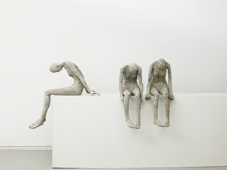 Three women sit on a white table with their heads bent.