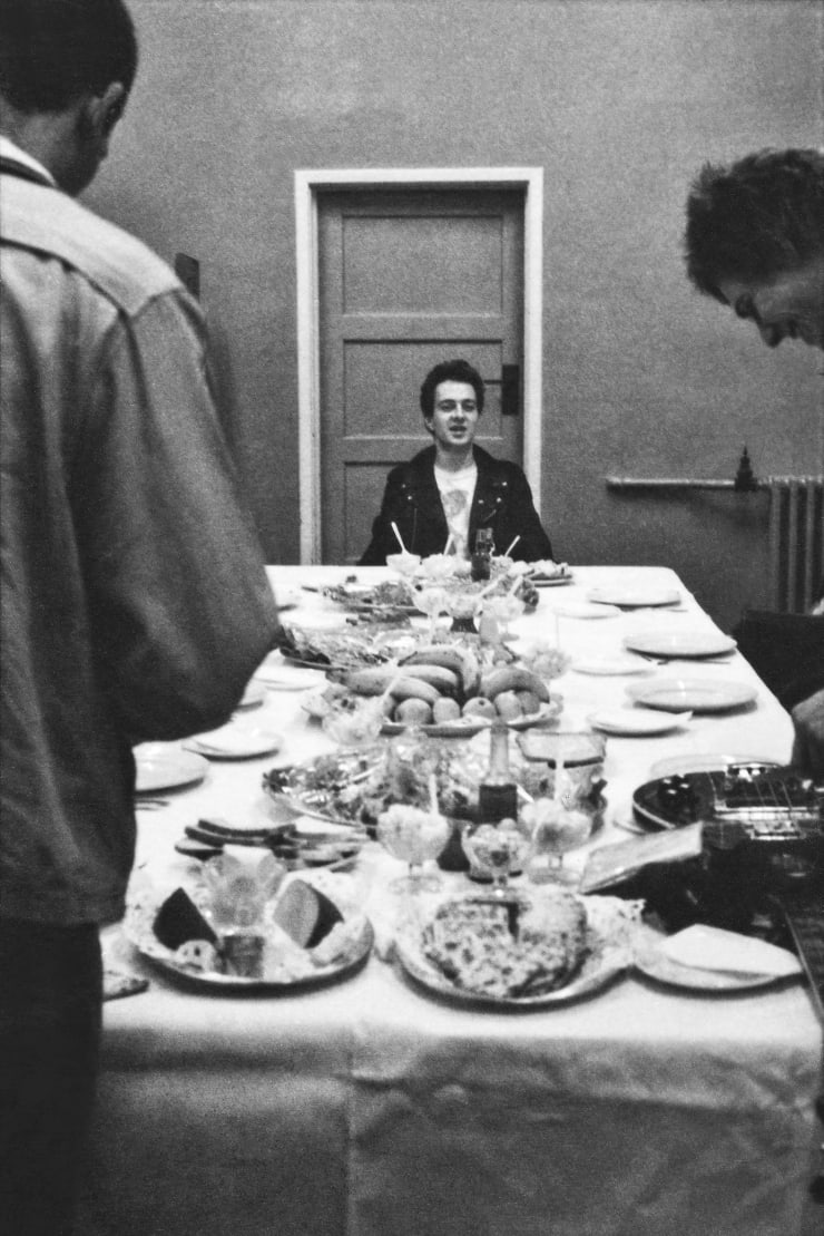 Caroline Coon The Clash. Joe Strummer at the head of the table before with the band’s ‘rider’ spread. [Somewhere] on the White Riot’ tour., 1977 Archival Pigment Print 42 x 29.7 cms 16 1/2 x 11 3/4 ins