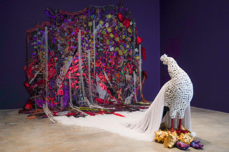 Ebony G. Patterson when the land is in plumage..., 2020 Glitter, Glue, Beads, plaster, conch shells, gold leaf, porcelain, paint, trimmings, jewelry, embellishments, fabric, jacquard tapestry and paraffin wax Overall dims: 9 x 16. 4 x 10.3 ft Tapestry: 9 x 12.9 x 10.3 ft Peacock on Conch Shells Dims: 3.7 x 6 x 2 ft