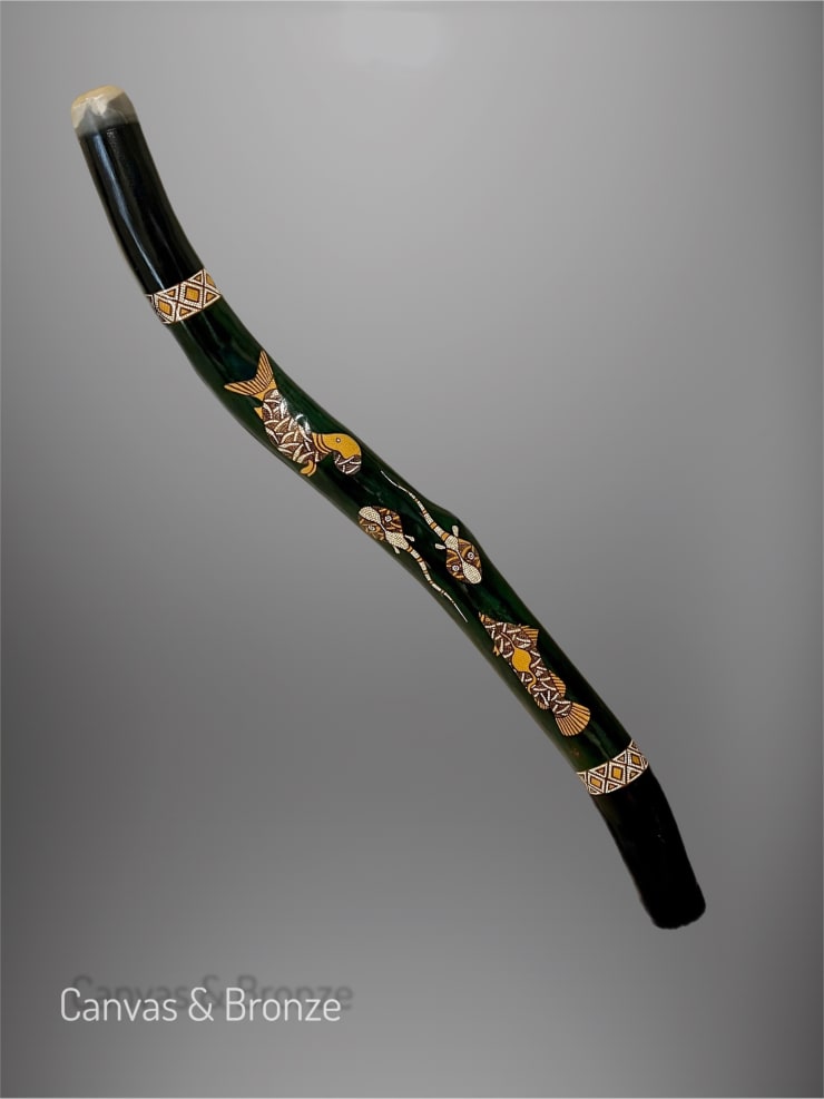 A dark green didgeridoo featuring intricate Aboriginal-style patterns and animal motifs in earthy tones, displayed against a neutral background.