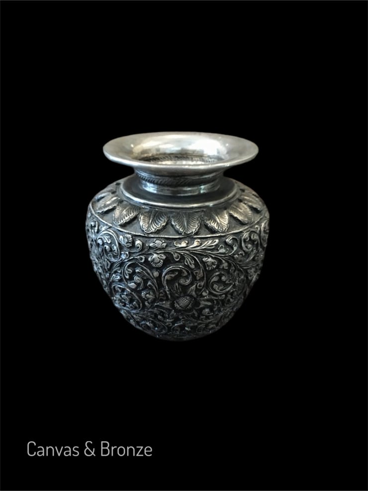 Ornate silver vase with intricate floral engravings against a black background.
