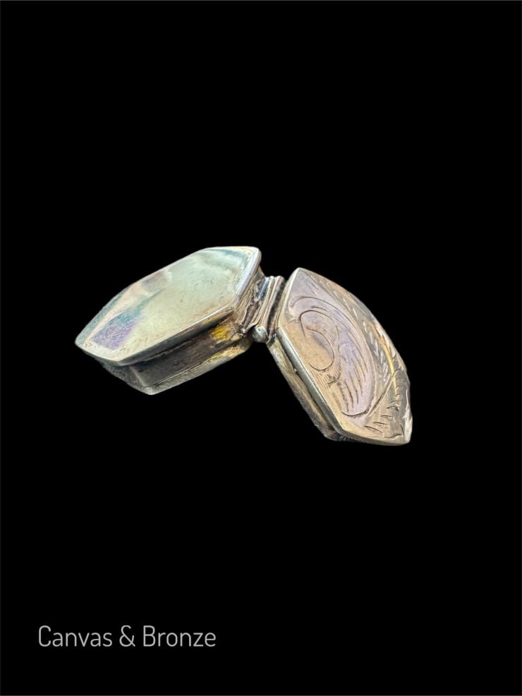 Antique silver locket with intricate engravings on a black background.