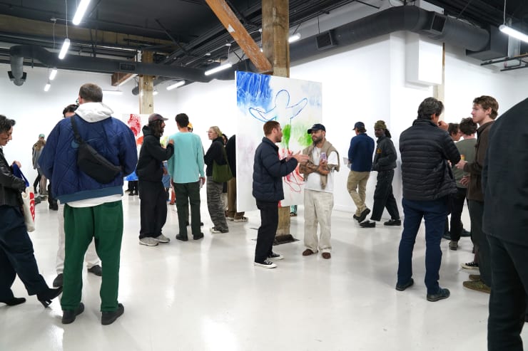 photograph of the gallery with paintings on the walls and a crowd of people inside