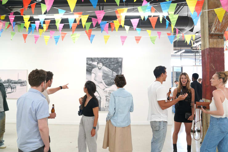 photograph of the gallery with paintings on the walls and a crowd of people