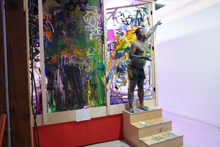 photo of the artist covered in paint standing on the steps of their "paint aquarium"