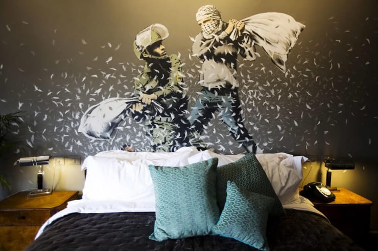 A painting by Banksy of an Israeli border police officer and a Palestinian man having a pillow fight above the bed in one of the rooms in the Walled Off Hotel