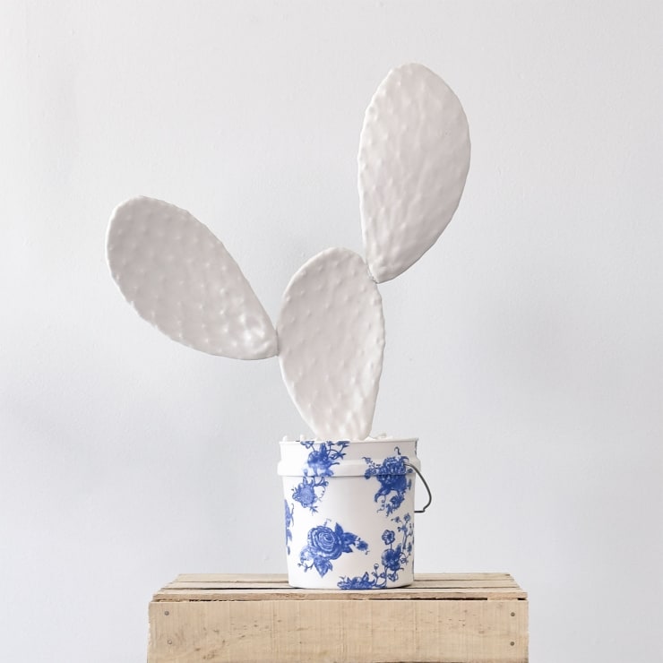 Porcelain sculpture by Brock DeBoer of a white cactus sitting in a cobalt blue toile pattern porcelain bucket sitting on a wooden box