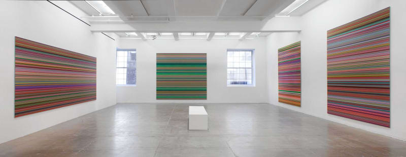 Four paintings, two on separate walls, three with a mix of primarily red vertical stripes among other colors; one with primarily green vertical stripes