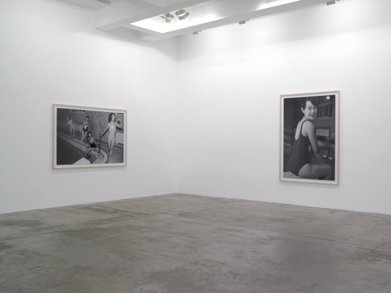 Two framed black and white photographs hanging in the corner of the room: one of four women at the edge of a pool, and the second of a woman sitting on a diving board, smiling at the camera.